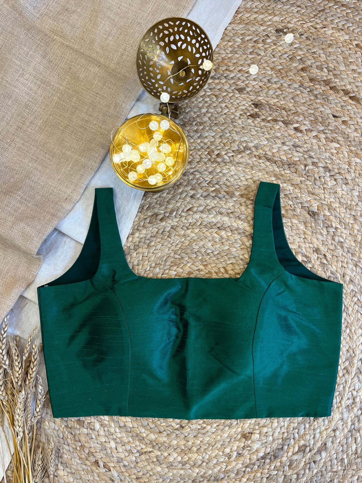 Elegant sleeveless green blouse with a structured neckline, displayed on a textured background, showcasing its rich fabric and minimalist design.